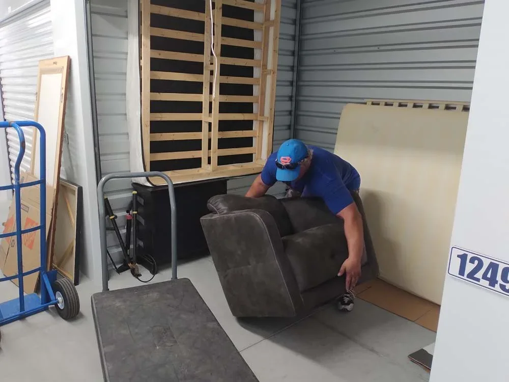 Two movers carrying a wrapped dresser down an exterior stairwell